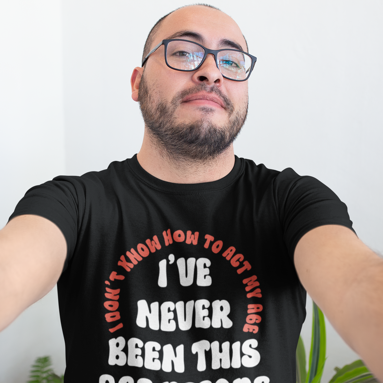 Man wearing a black t-shirt with text, standing against a white wall.