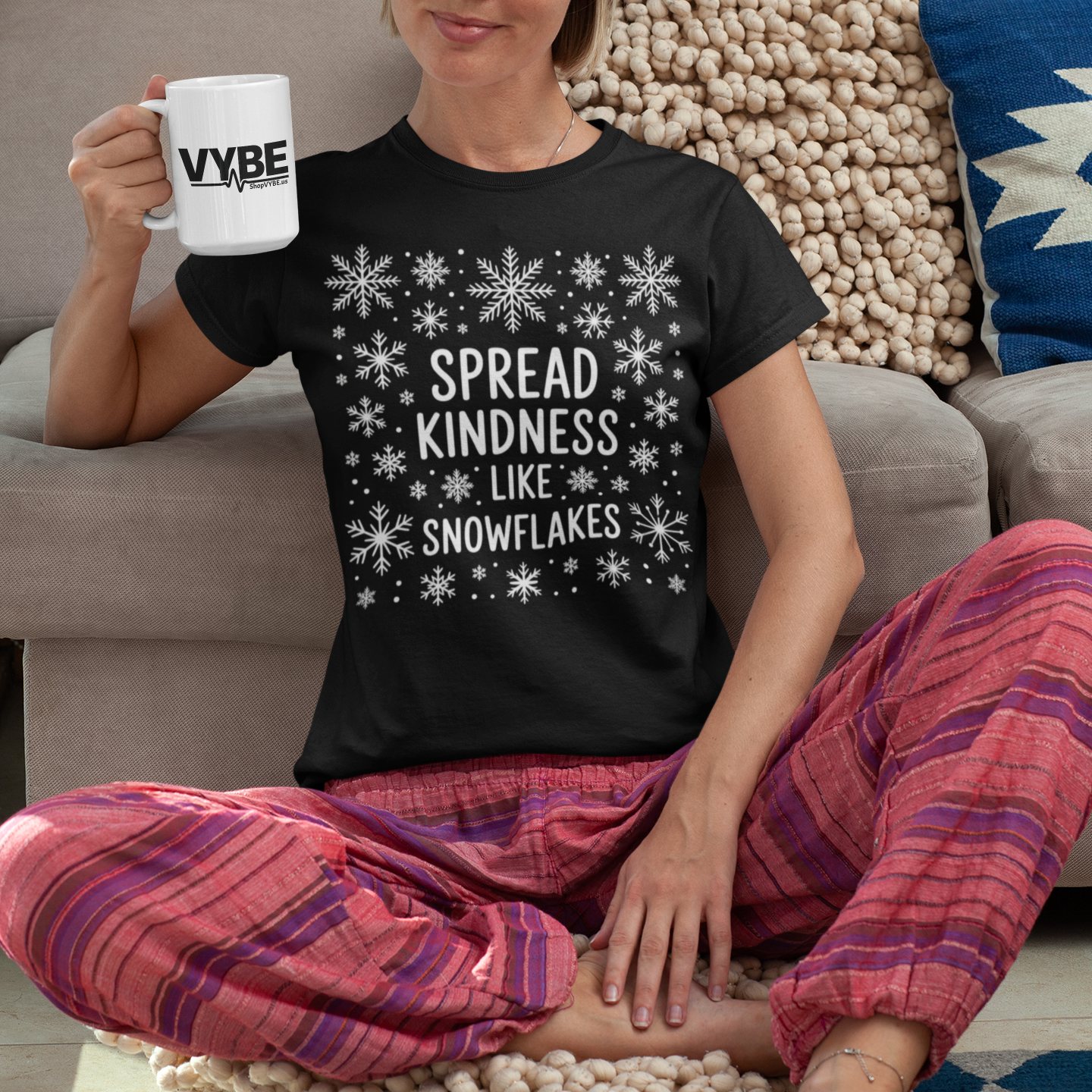 Person wearing a black t-shirt with 'Spread Kindness Like Snowflakes' text, sitting on a colorful rug.