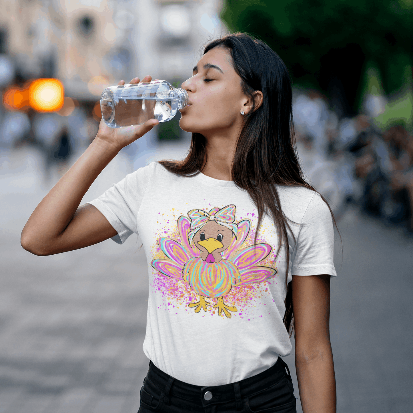 Woman drinking water outdoors wearing a t-shirt with a colorful turkey design.