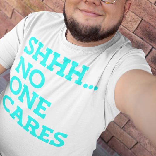 Person wearing a white t-shirt with teal text 'SHHH... NO ONE CARES' against a brick wall.