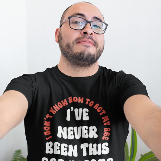 Man wearing a black t-shirt with text, standing against a white wall.