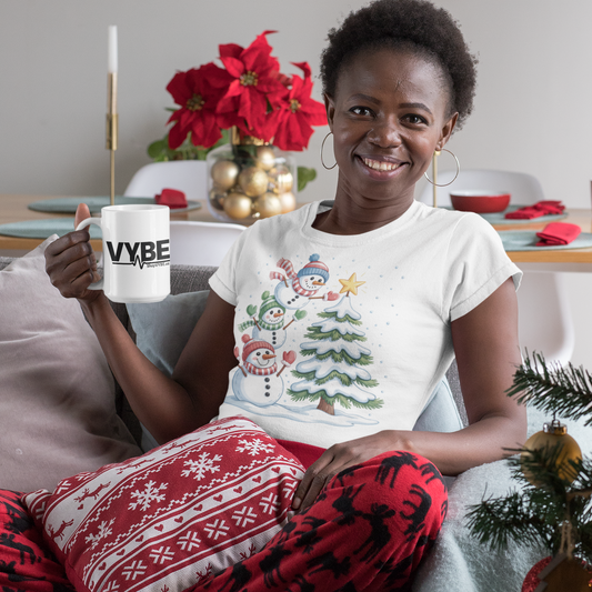 Woman sitting on a couch holding a mug with a Christmas-themed shirt and red pants, surrounded by festive decorations.