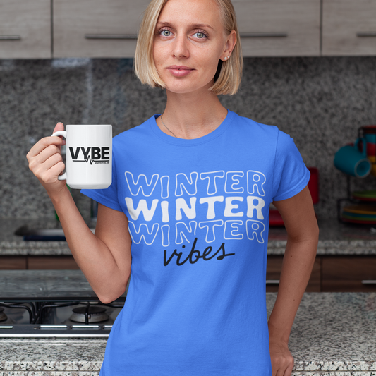 Woman in a kitchen wearing a blue t-shirt with 'Winter Vibes' text and holding a white mug.
