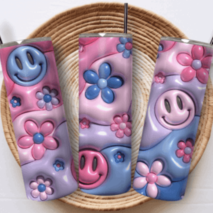Three colorful tumblers with floral and smiley face designs on a woven mat.