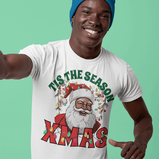 Person wearing a white t-shirt with a Christmas design and text, pointing at the camera on a green background.