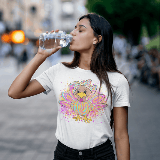 Woman drinking water outdoors wearing a t-shirt with a colorful turkey design.
