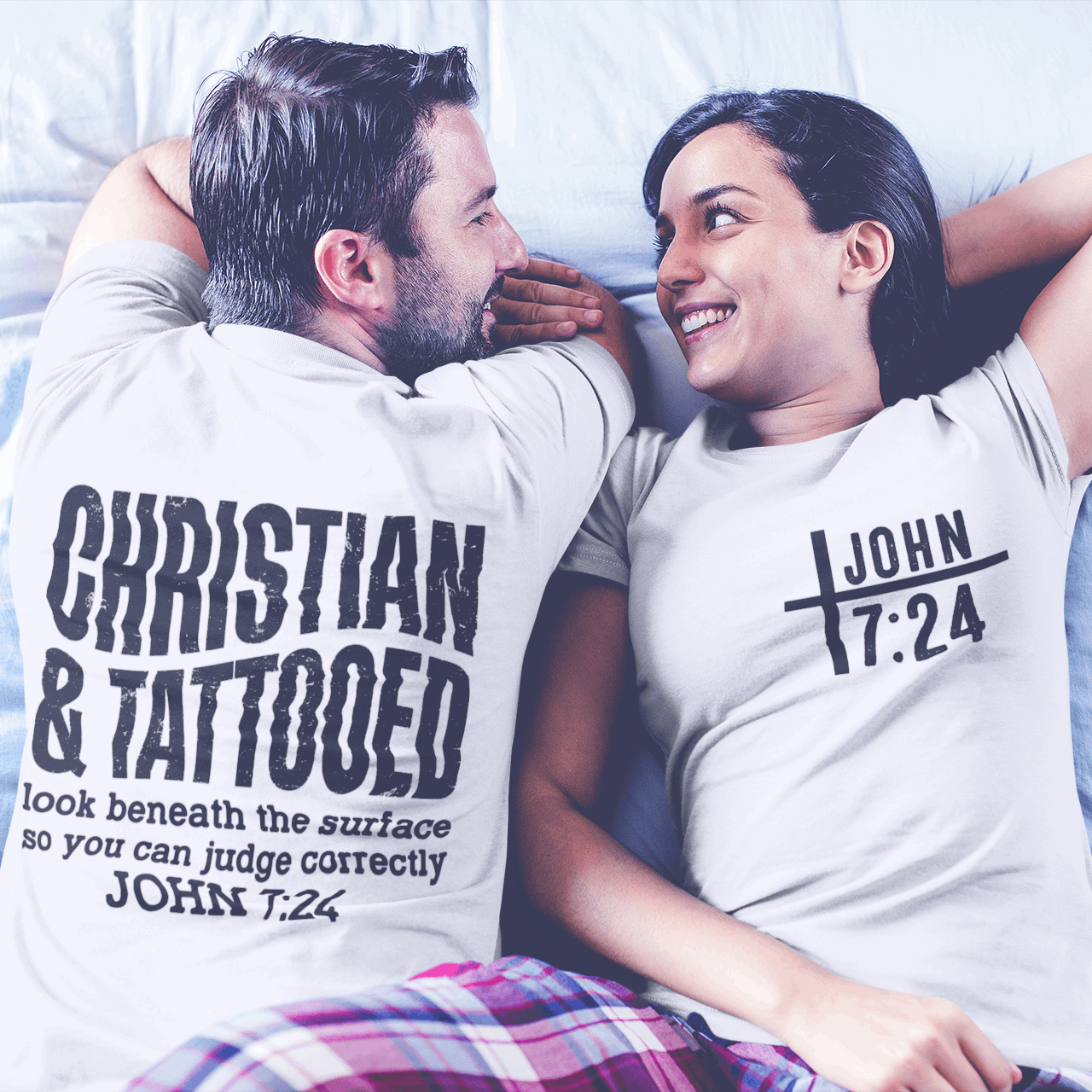 Two people lying on a bed wearing t-shirts with text.