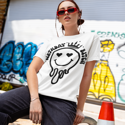 Person wearing a white t-shirt with a smiley face design in an urban setting with graffiti.