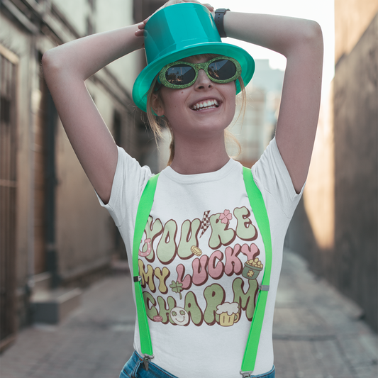 Person wearing a white t-shirt with colorful text, green suspenders, and a teal hat in an urban setting.