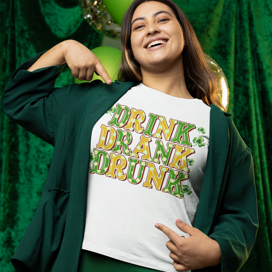 Person wearing a white t-shirt with 'Drink Drone Drunk' text in front of green curtains.