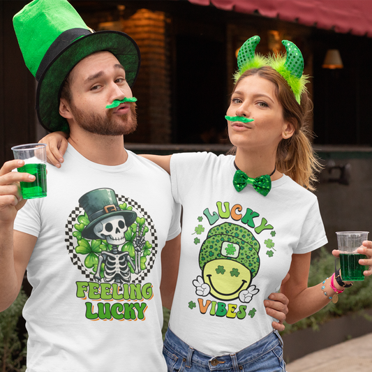 Two people wearing festive shirts and accessories, holding green drinks, outdoors.