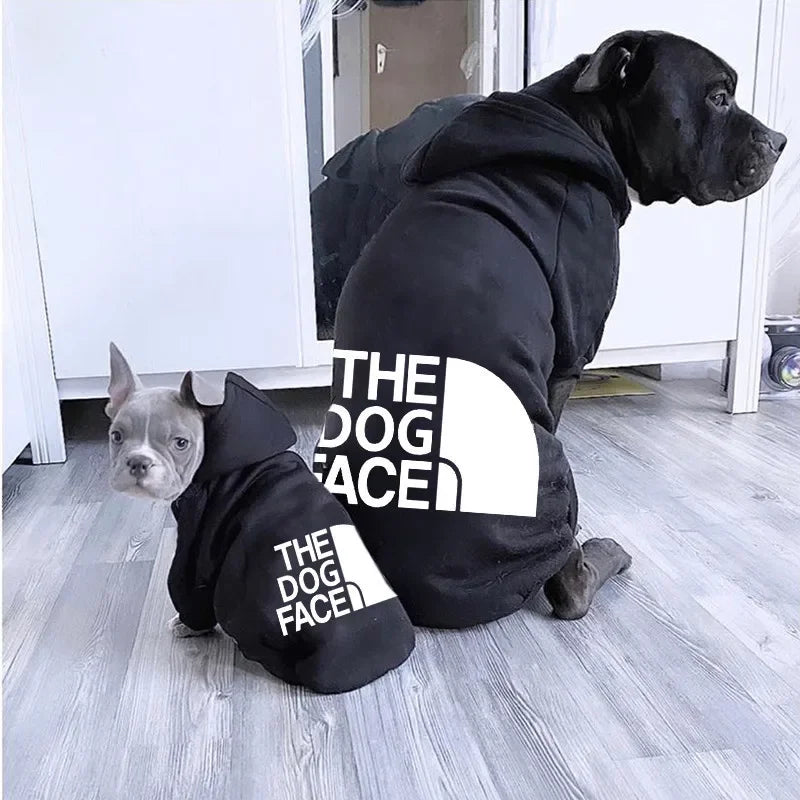 Two dogs wearing black hoodies with 'The Dog Face' logo on a wooden floor.