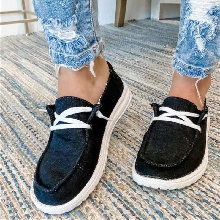 Black loafers with white laces worn with ripped jeans on a patterned carpet.