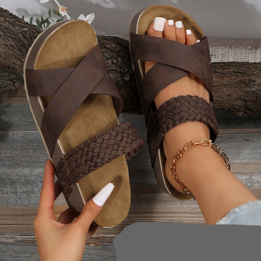 Brown sandals with braided straps worn on a wooden floor
